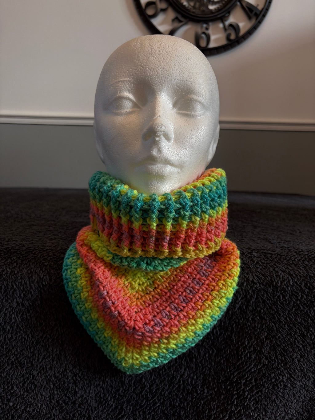 knit triangle neck warmer with a gold tag on a mannequin head against a dark textured background
