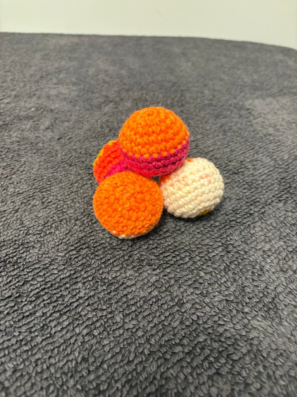 Three crocheted balls in orange, pink, and white on a textured gray surface.