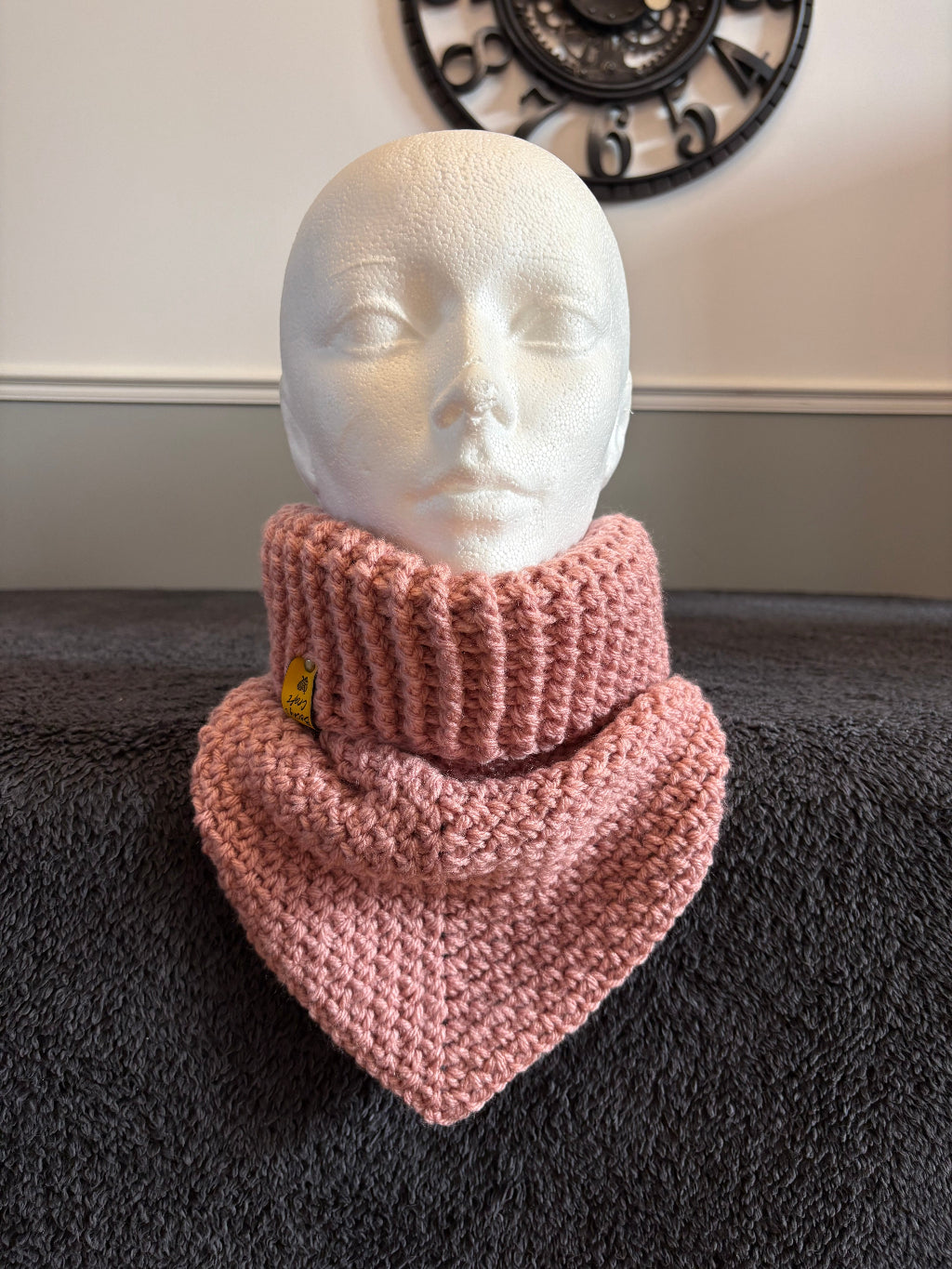 knit triangle neck warmer with a gold tag on a mannequin head against a dark textured background