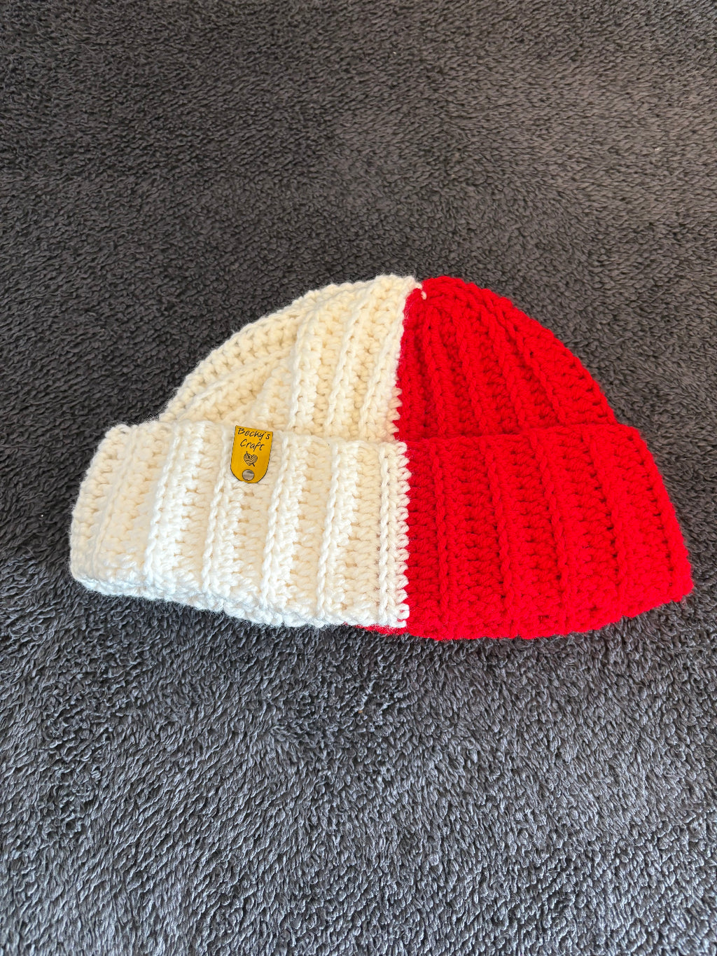 Crocheted hat with red top and beige bottom on a gray surface