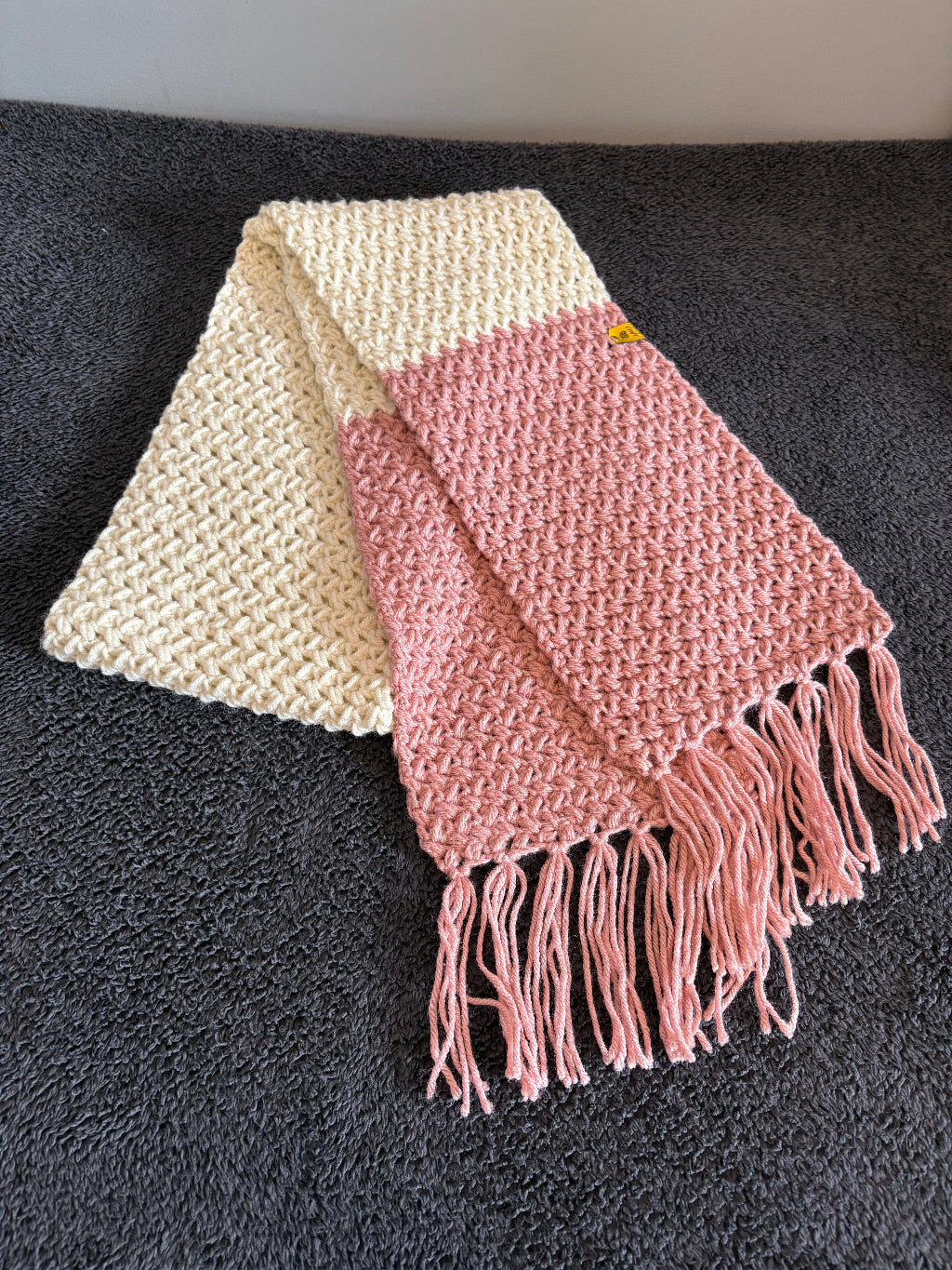Pink and beige knitted scarf with fringes on a dark surface