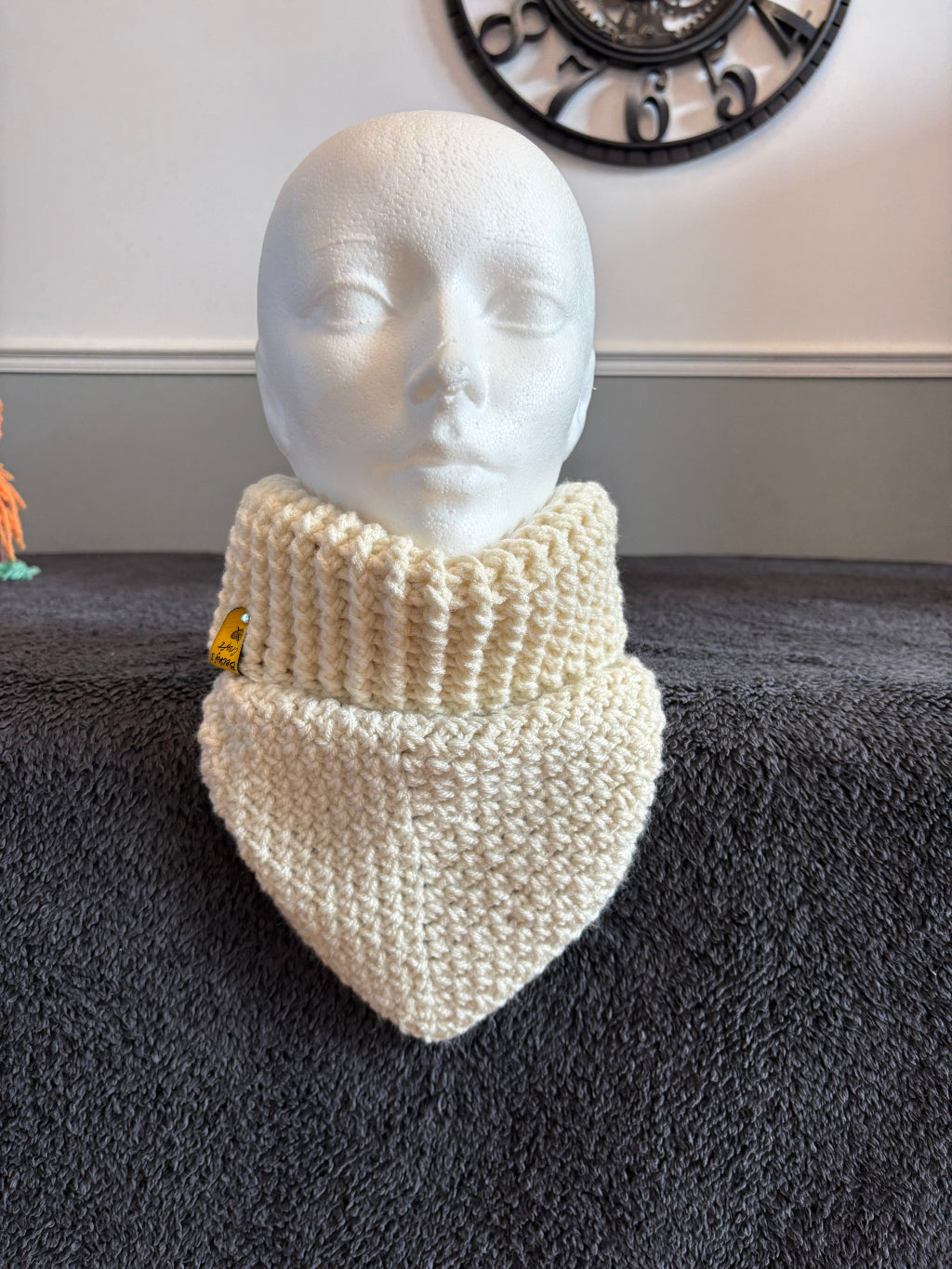 knit triangle neck warmer with a gold tag on a mannequin head against a dark textured background