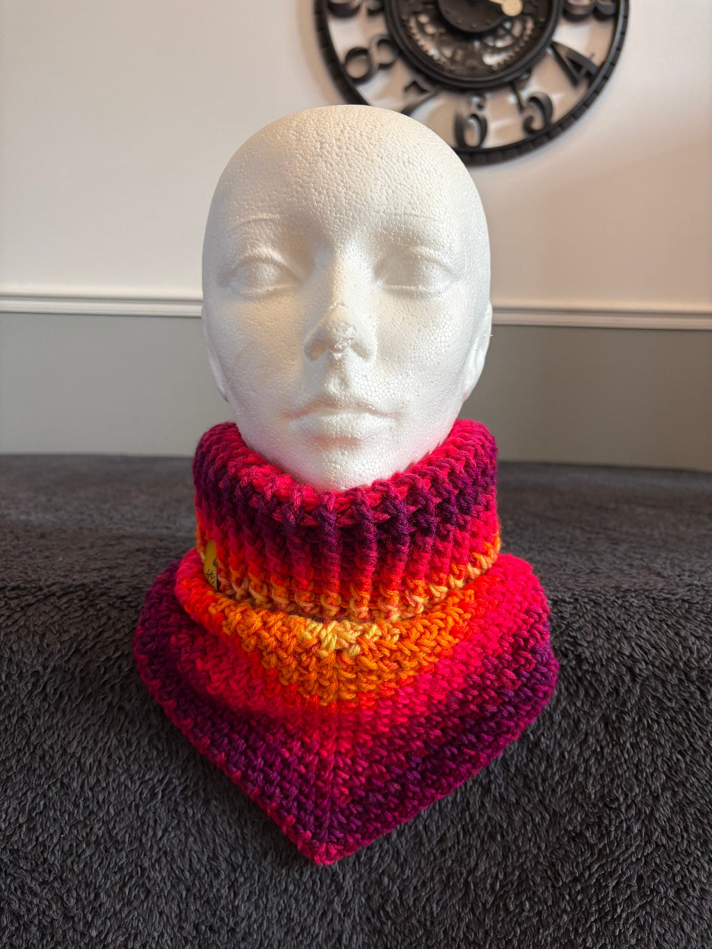 knit triangle neck warmer with a gold tag on a mannequin head against a dark textured background
