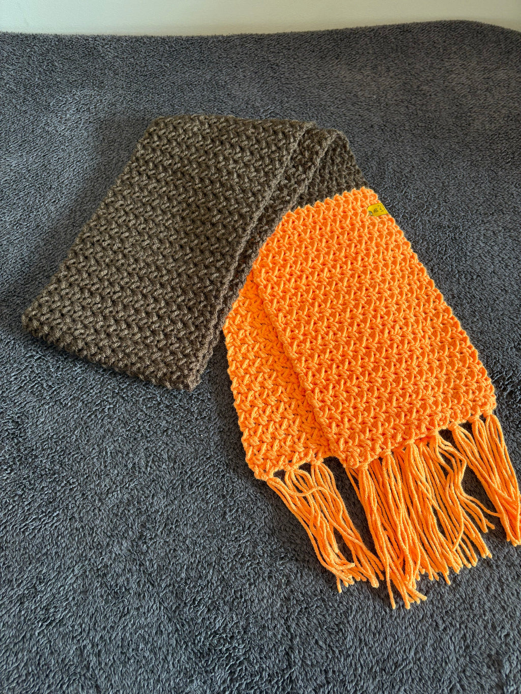 Orange and brown knitted scarf with fringes on a gray surface