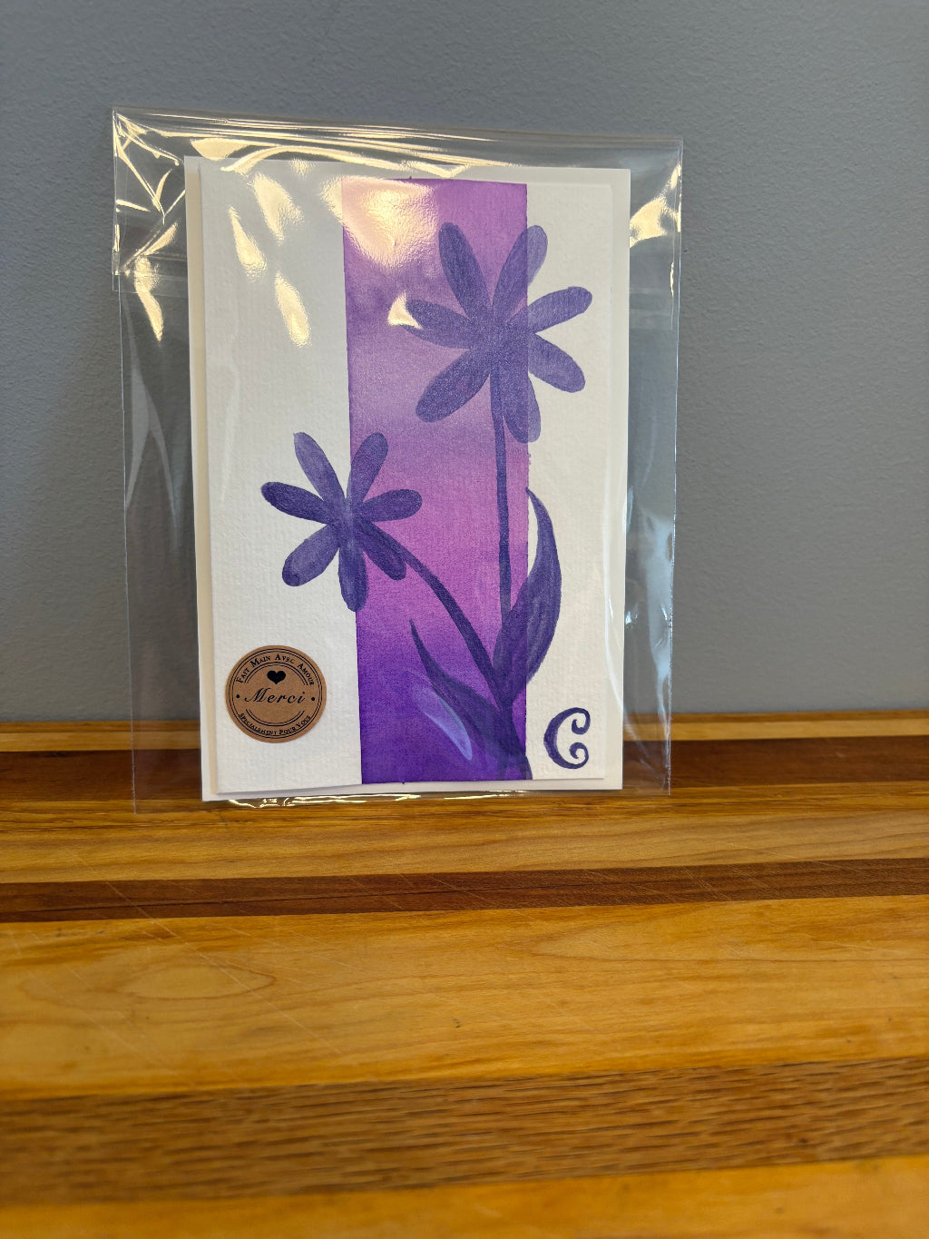 Card with purple floral design in clear packaging on a wooden surface