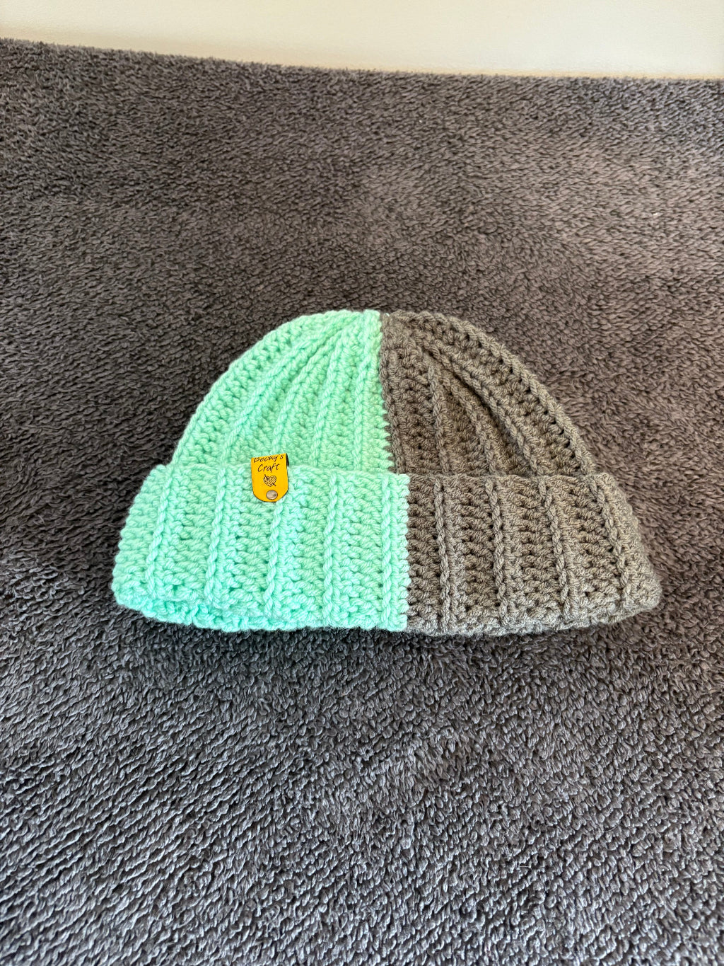 Crocheted beanie with half and half color pattern on a textured surface