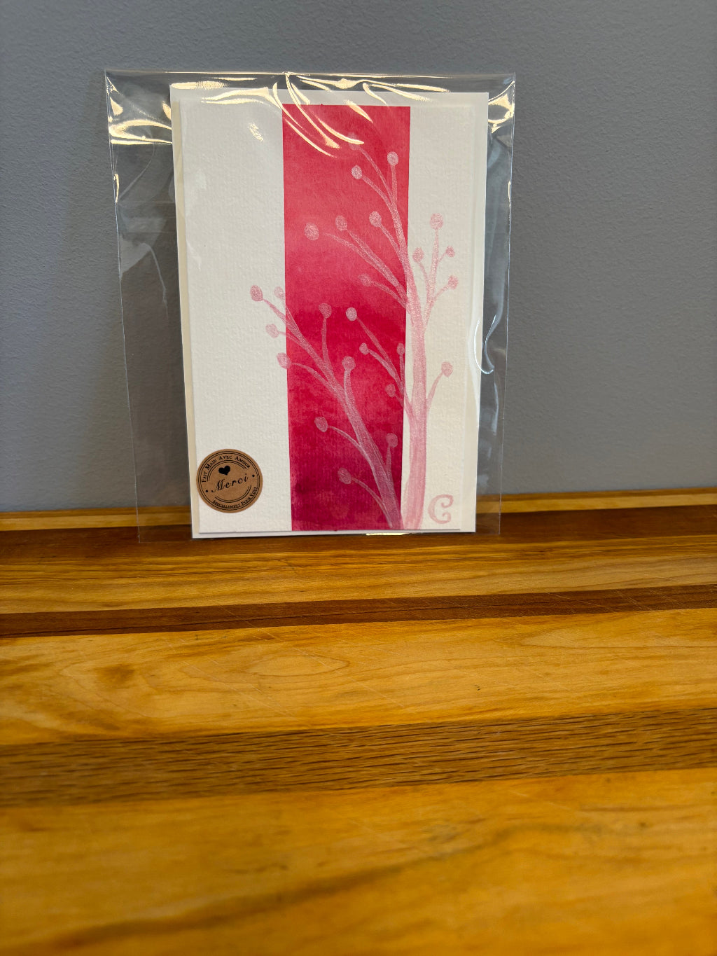 Card with red and white design in clear packaging against a wooden surface
