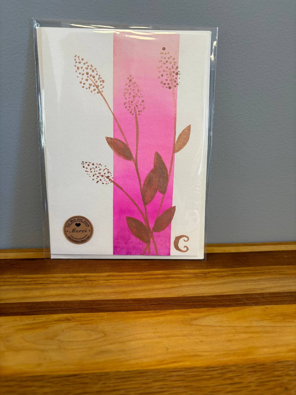 Card with floral design on a pink background, placed on a wooden surface with a gray wall in the background.