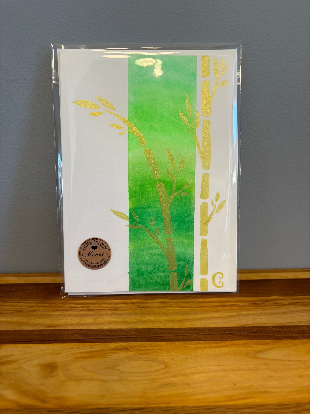 Packaged card with green and yellow design on a wooden surface and gray wall background