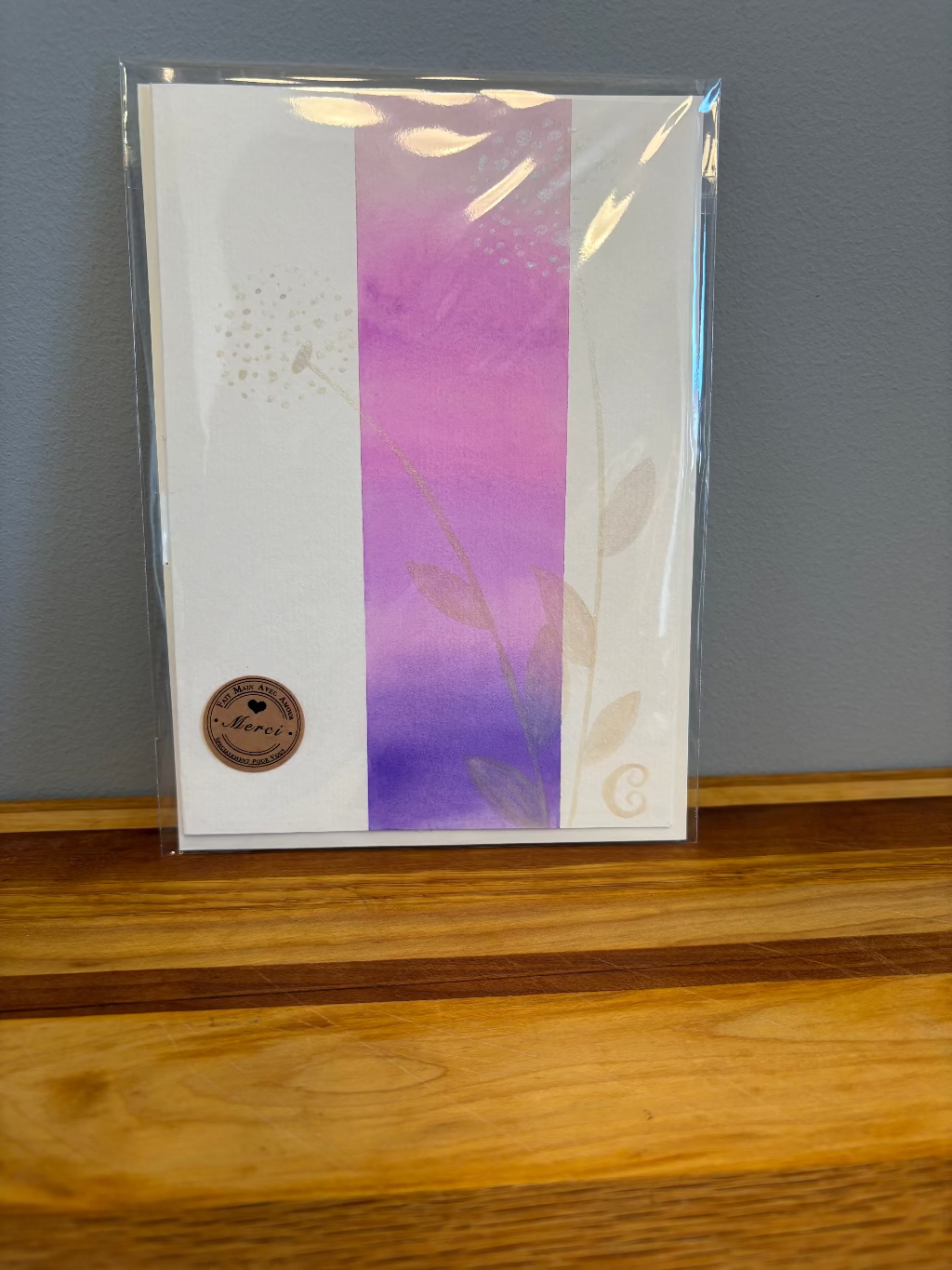 Card with purple gradient and floral design in clear packaging on a wooden surface.