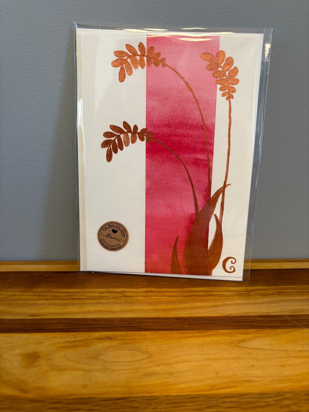 Card with floral design on a pink and white background, placed on a wooden surface.